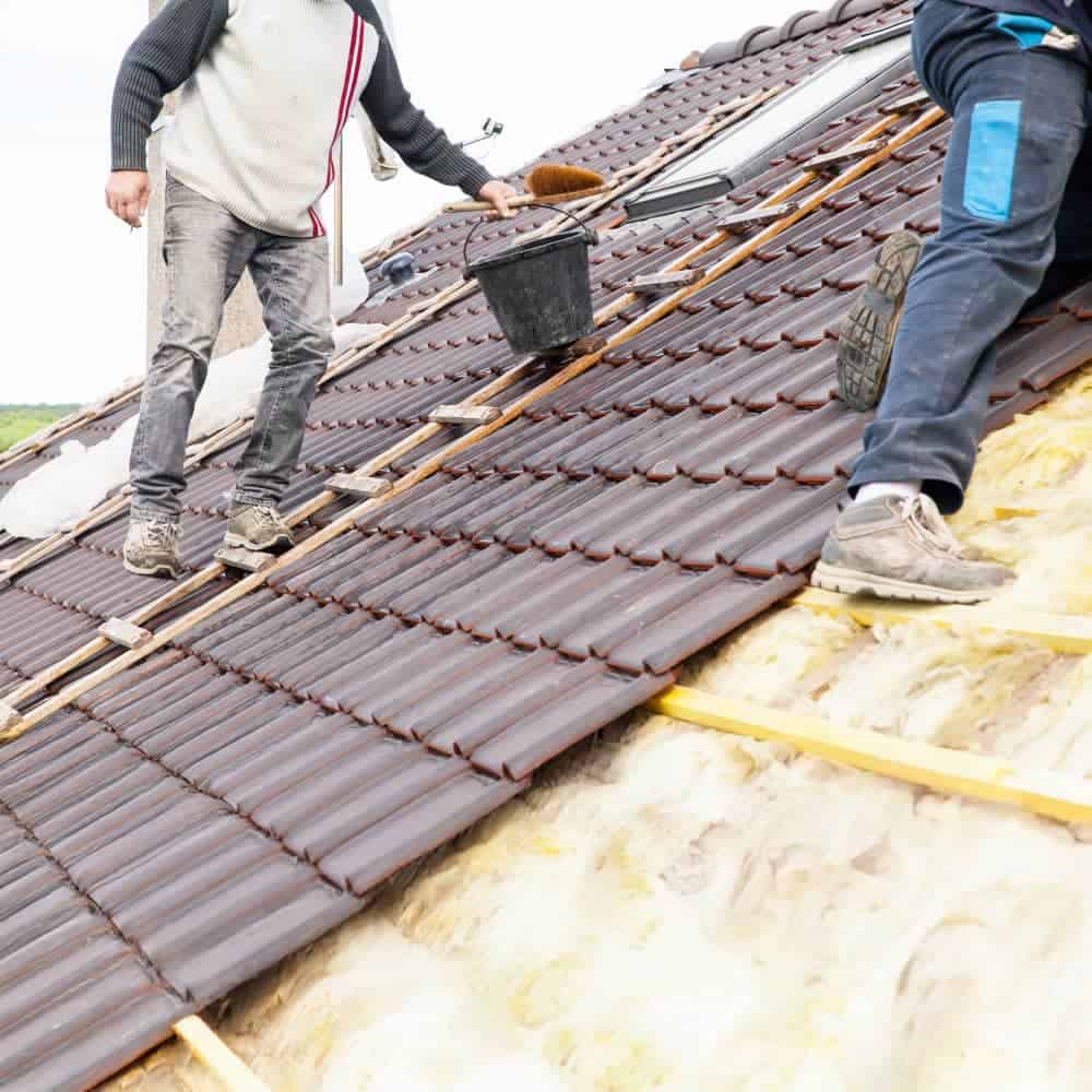 Roofing workers installing tiles on a sloped roof for home improvement.