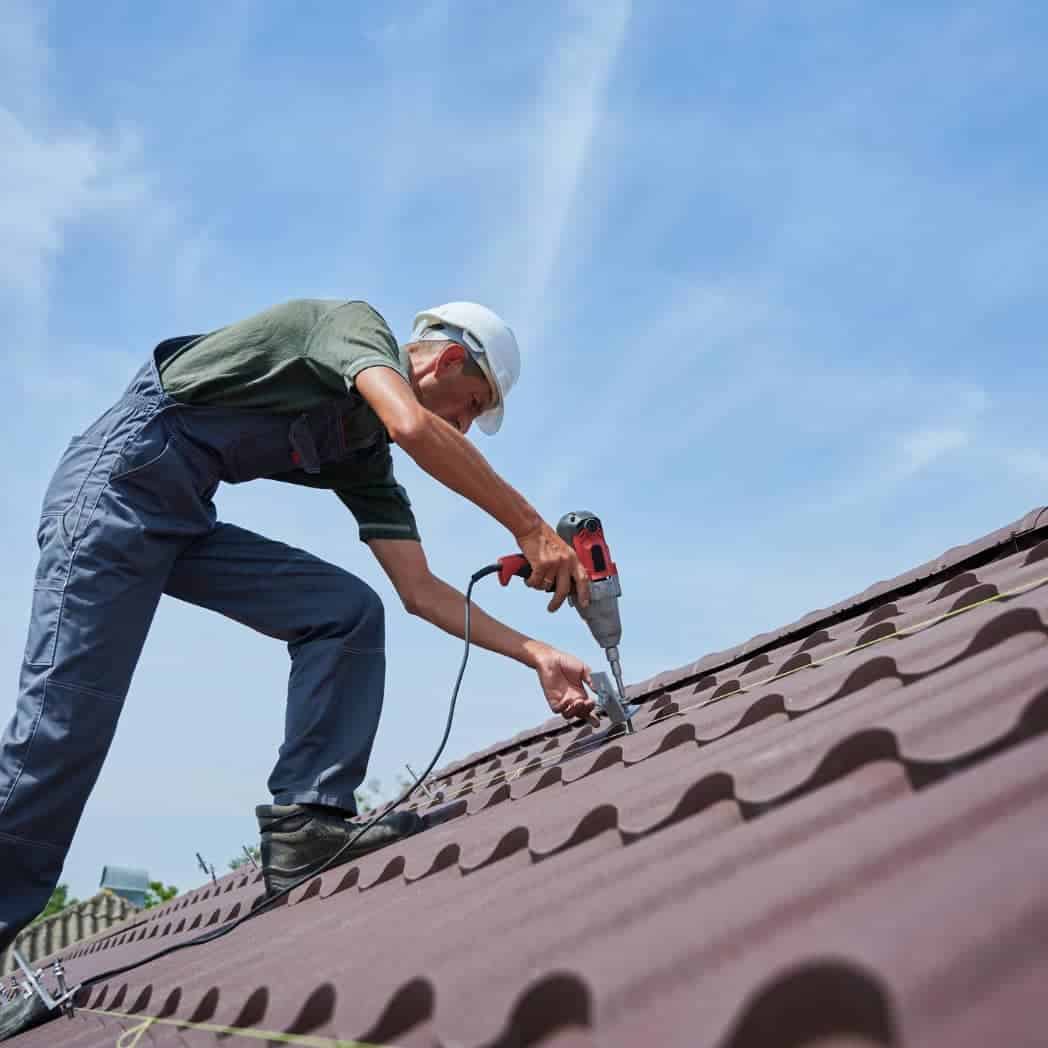 Roofing technician repairing roof with power drill on residential building.