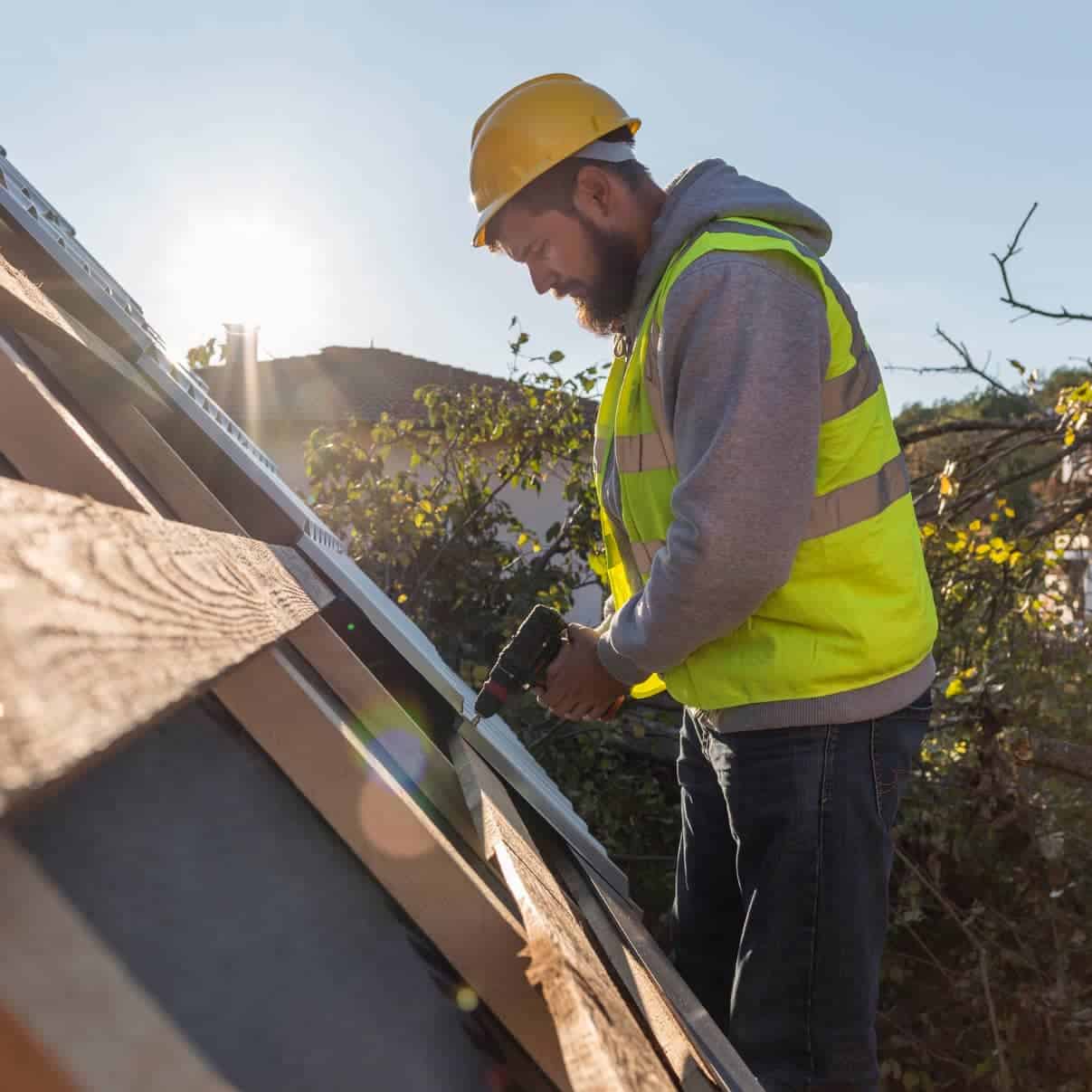 Roofing professional using a drill on a residential roof during installation.