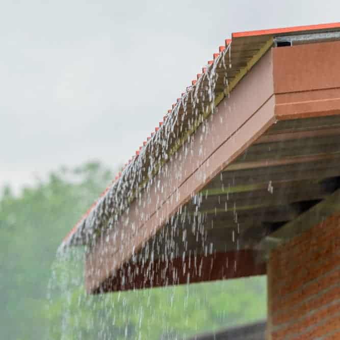 Close-up of rainwater gutter on residential roof with water flowing.