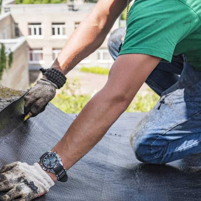 Worker installing roofing membrane on a building roof.
