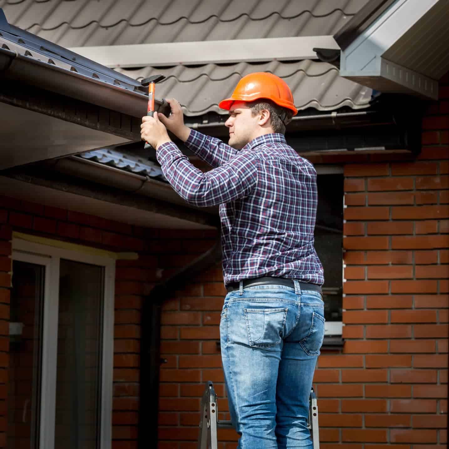 Roofing professional installing gutter on residential house.