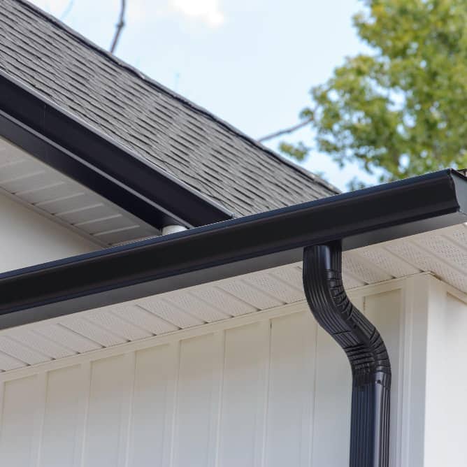 Close-up of black gutter and downspout on house roof.