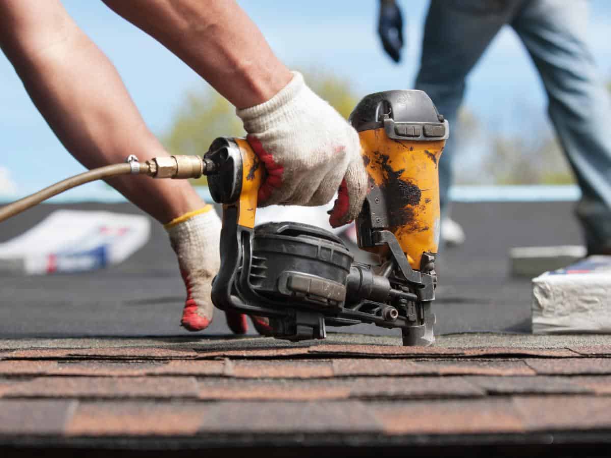 Worker using a nail gun to install roof shingles