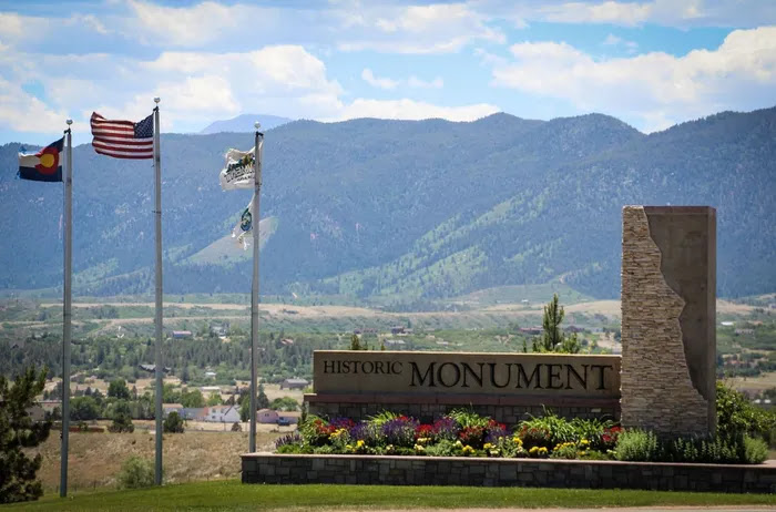 Historic Monument welcome sign with flags and mountains behind it in Monument, CO
