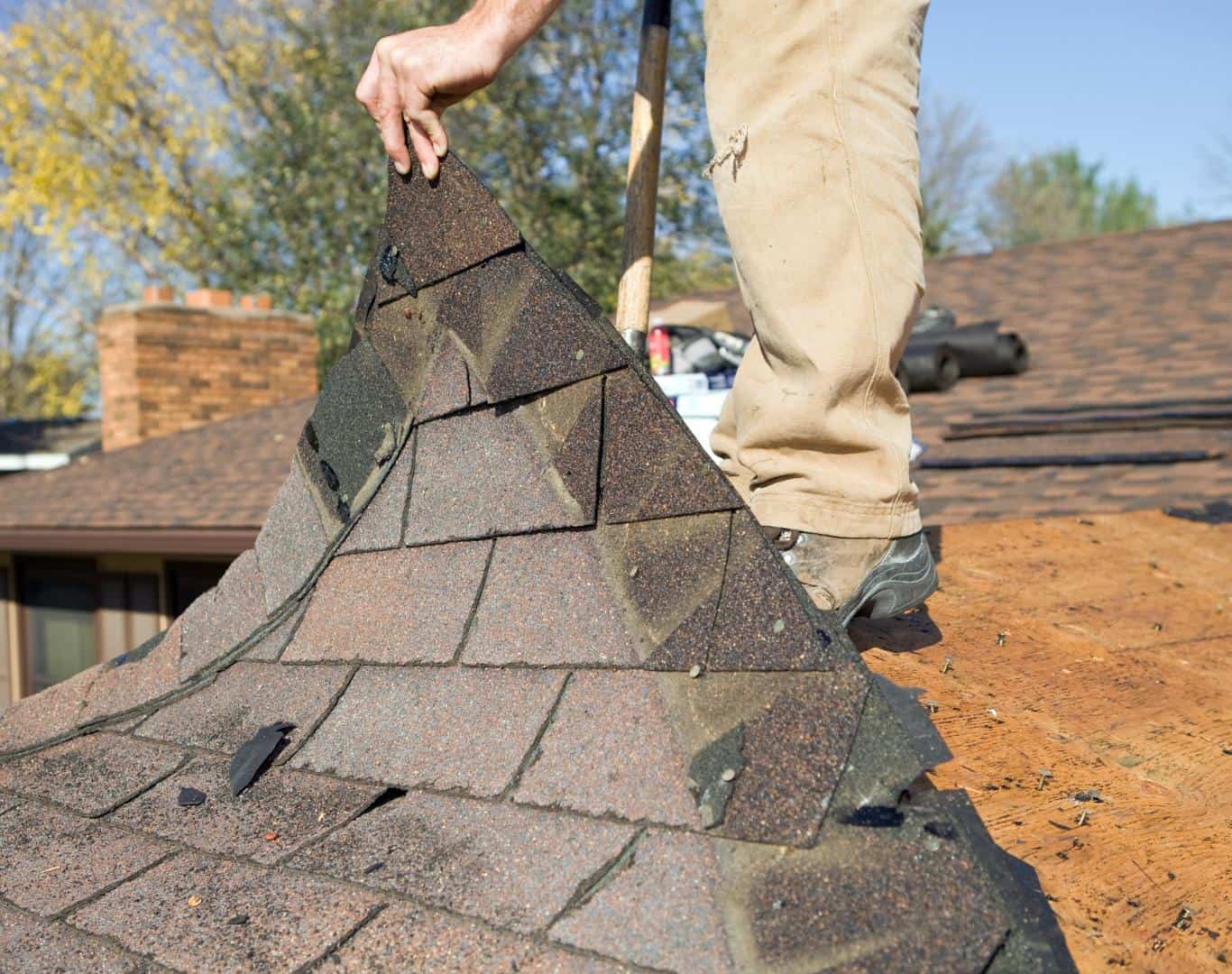 Roofer tearing off old asphalt shingles
